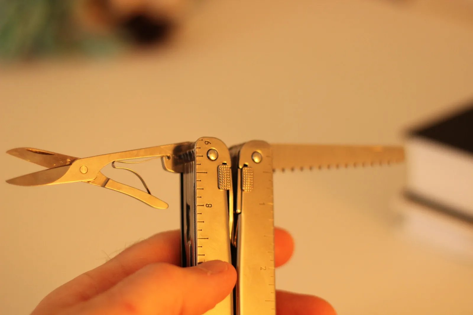 The Swiss Tool MX Clip held in folded-V configuration with the wood saw extended to the right and the scissors deployed at left, integrated rulers visible on both handles