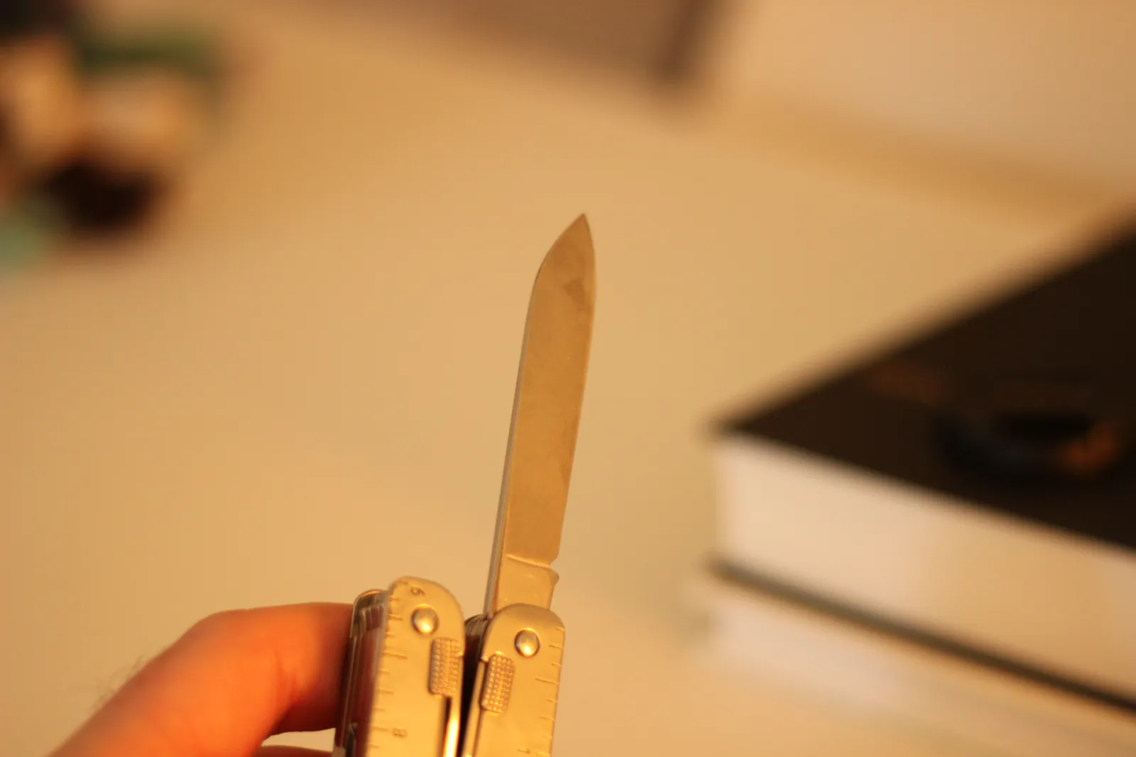 The Swiss Tool MX Clip's large blade extended and locked open shown from a higher angle against a soft-focus background of books on a workbench