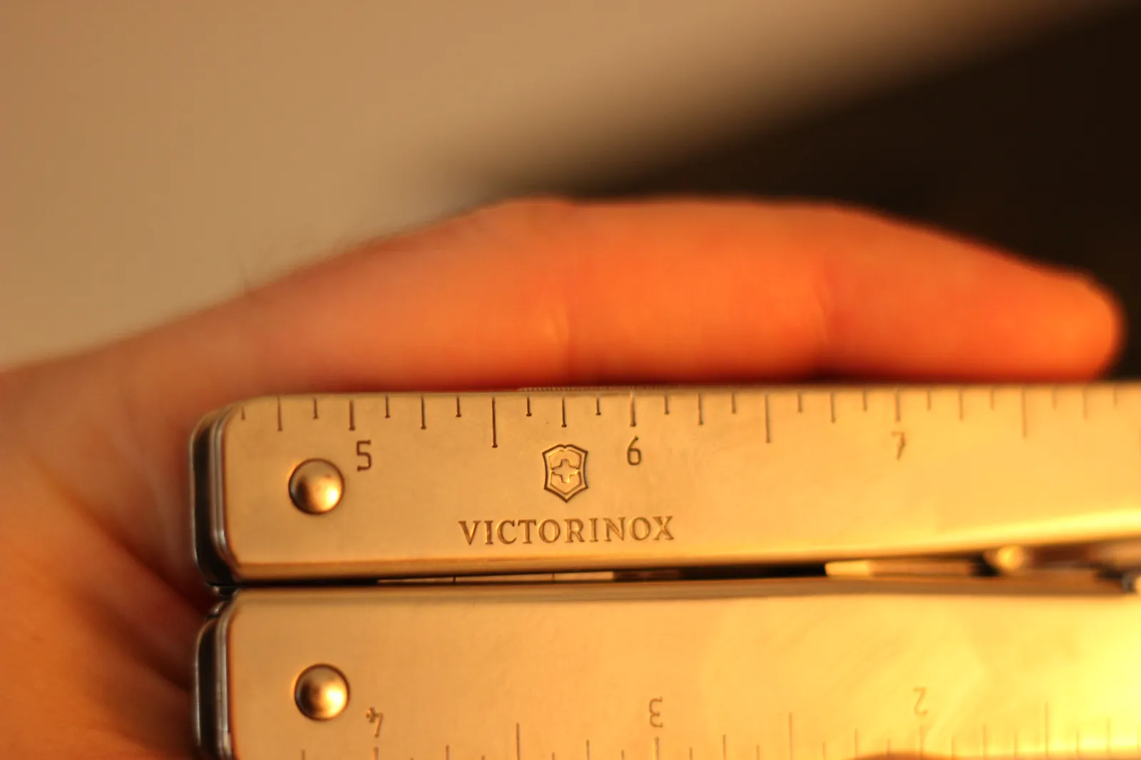A close-up of the Swiss Tool MX Clip handle showing the VICTORINOX shield and wordmark stamped into the steel along the ruler edge with a finger resting against the body