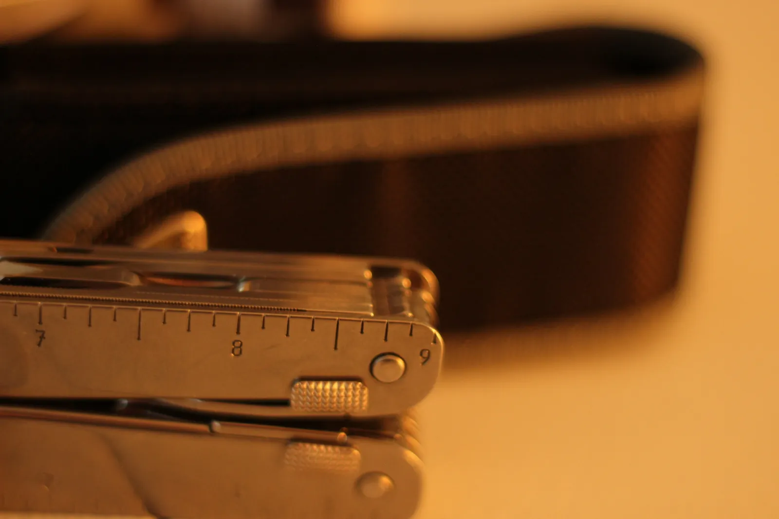The Swiss Tool MX Clip closed in profile beside its black nylon belt pouch showing the ruler markings on the handle back and the dual cordura pouch construction