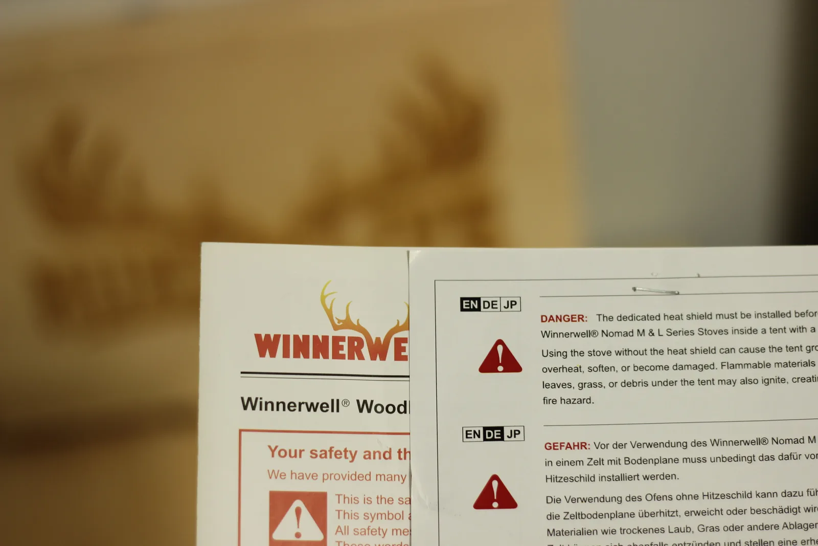 A printed safety sheet with a red DANGER heading reading that the dedicated heat shield must be installed before using Nomad M and L series stoves inside a tent with a groundsheet