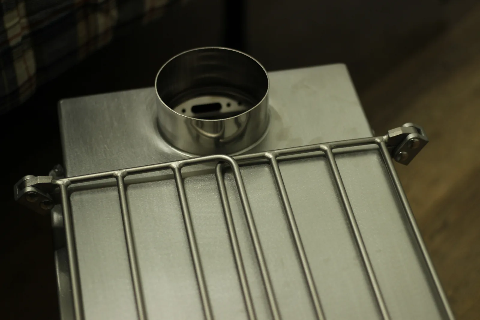 The stove from above showing the flat brushed stainless top plate, the swaged flue collar, and the wire side rack folded across it