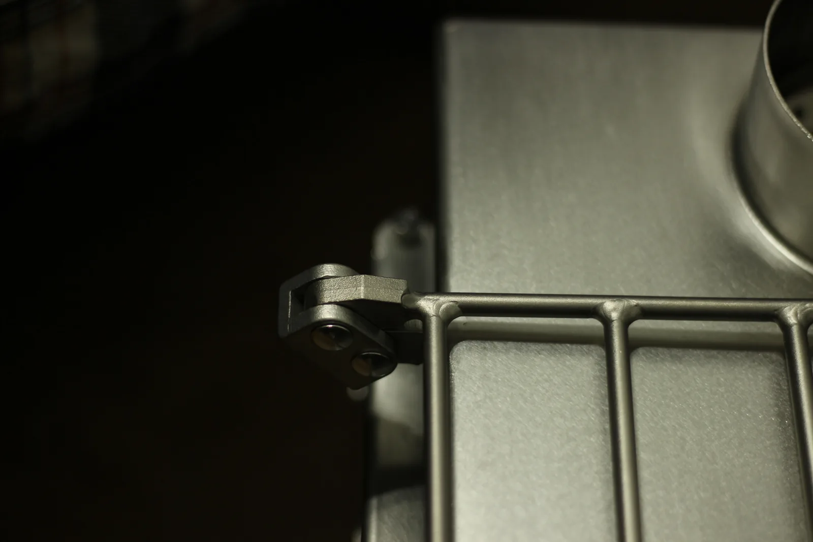 A cast stainless bracket on the stove body holding the wire side rack, secured with two bolts