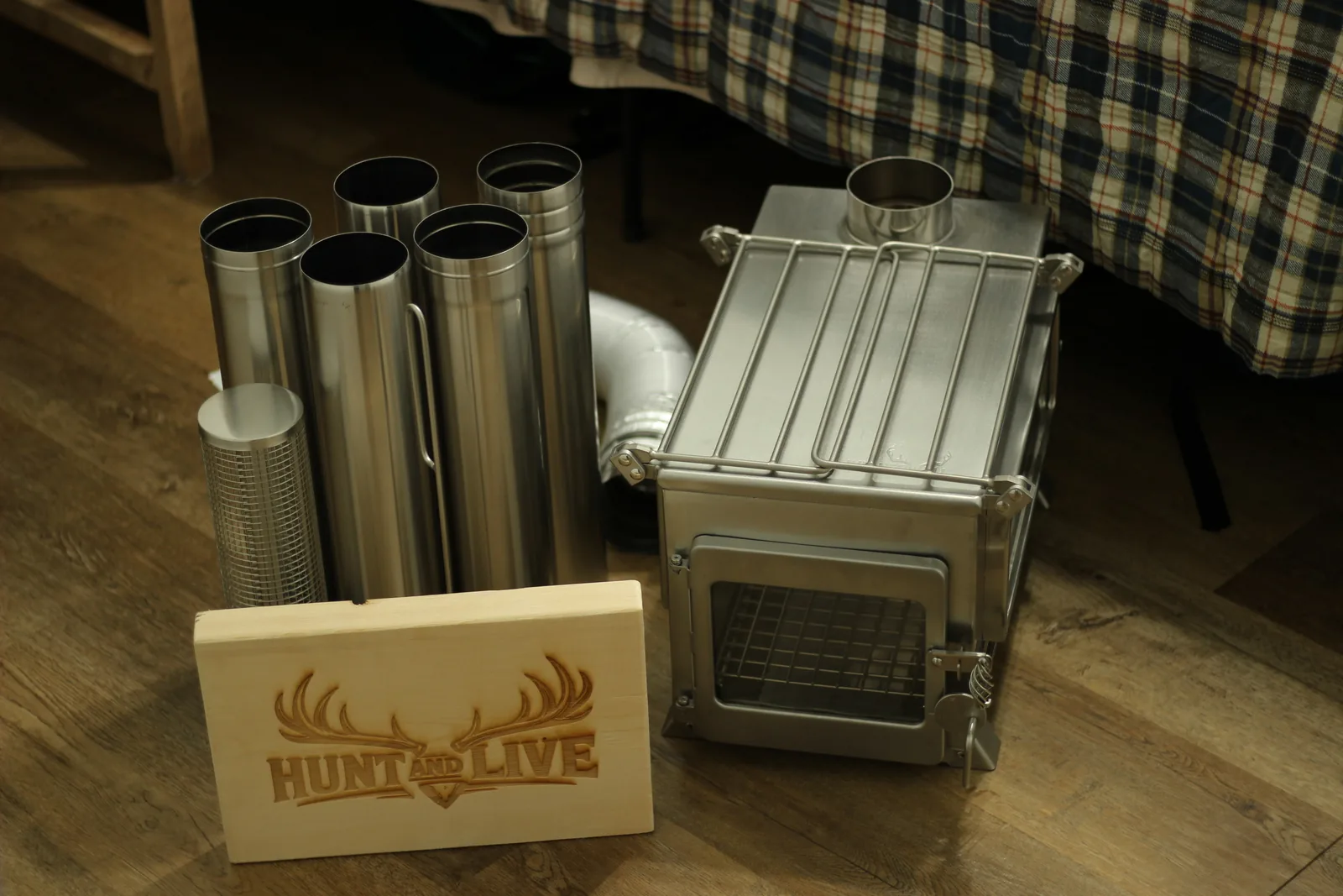 The complete stove kit laid out on a wooden floor: the stove body, five chimney sections, spark arrestor and the external air hose, with the Hunt and Live engraved plaque for scale