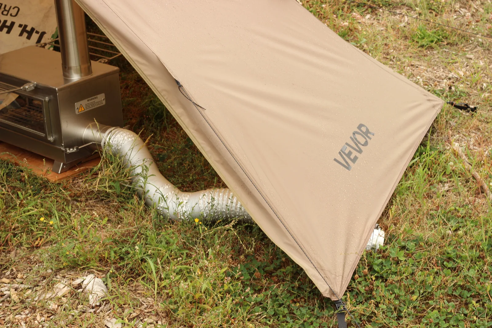 The flexible silver external air duct emerging from under the tent wall onto the grass outside