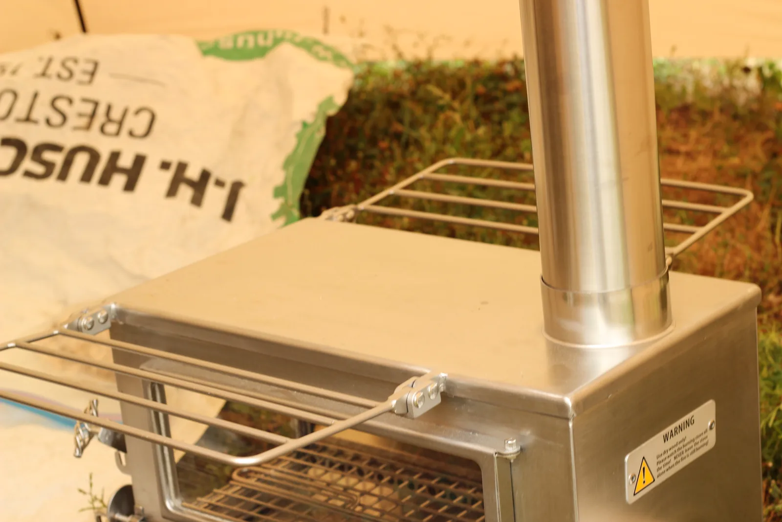 The stove set up on plywood at the edge of the tent with its chimney rising and the wire rack extended