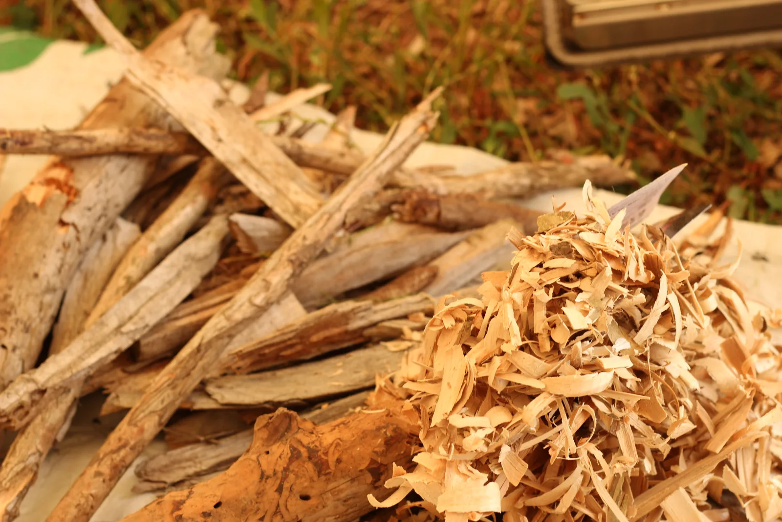 A pile of split kindling and a heap of pale wood shavings on the ground