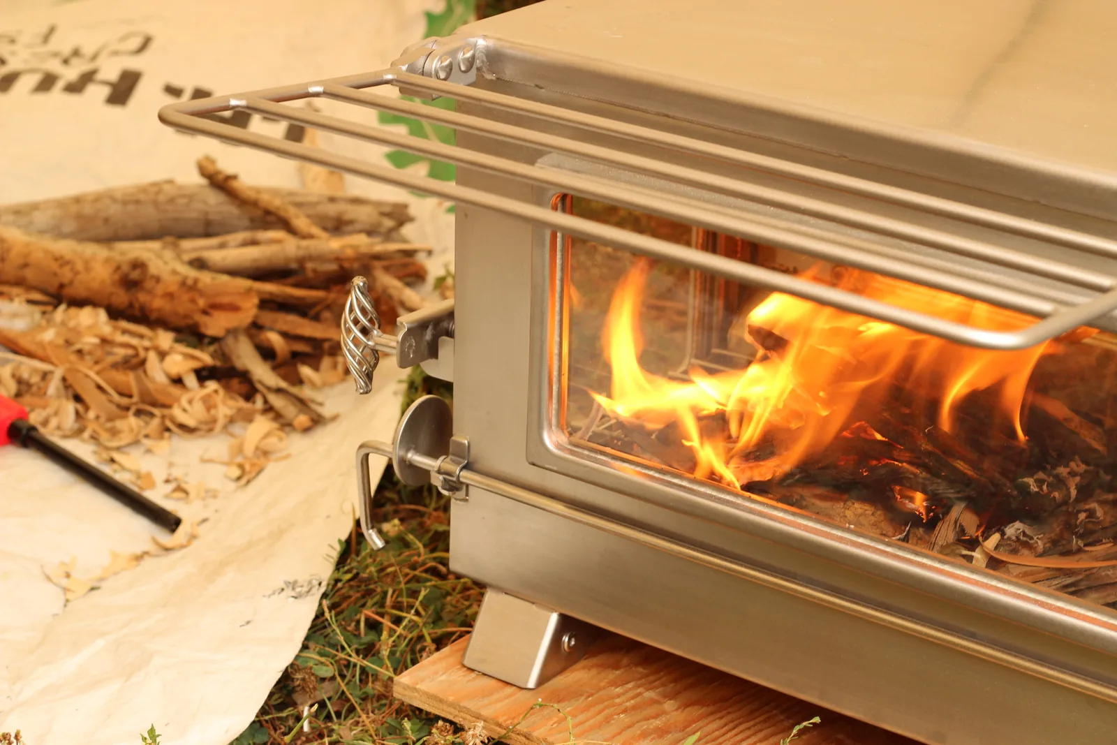 The burning stove with a pile of split wood beside it on a tarp