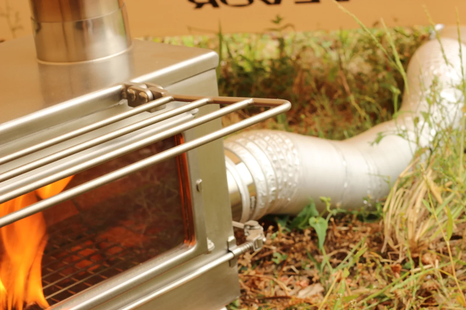 The external air duct at the stove's intake port with flames visible through the glass beside it