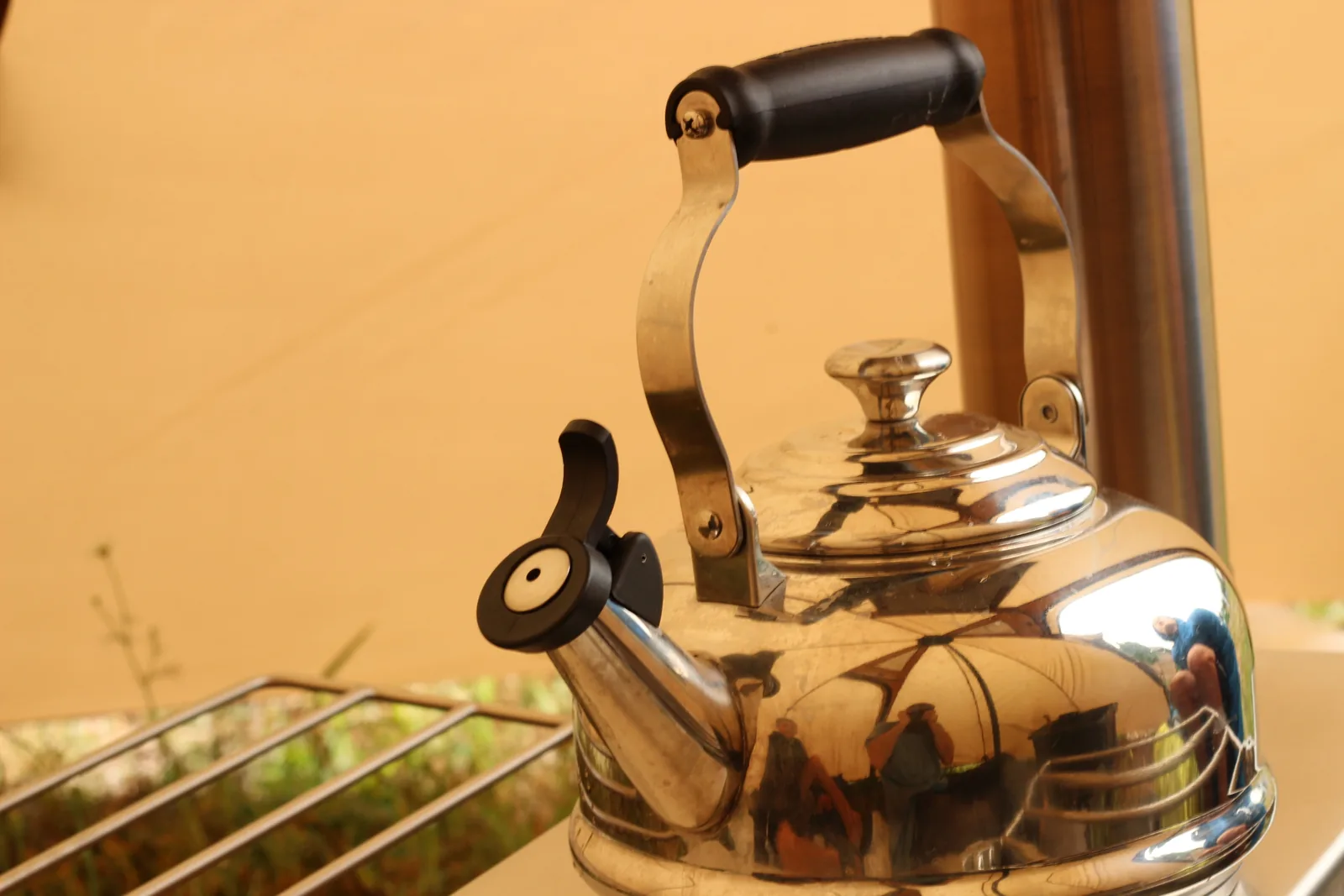 A polished stainless whistling kettle sitting on the stove's top plate with the chimney rising behind