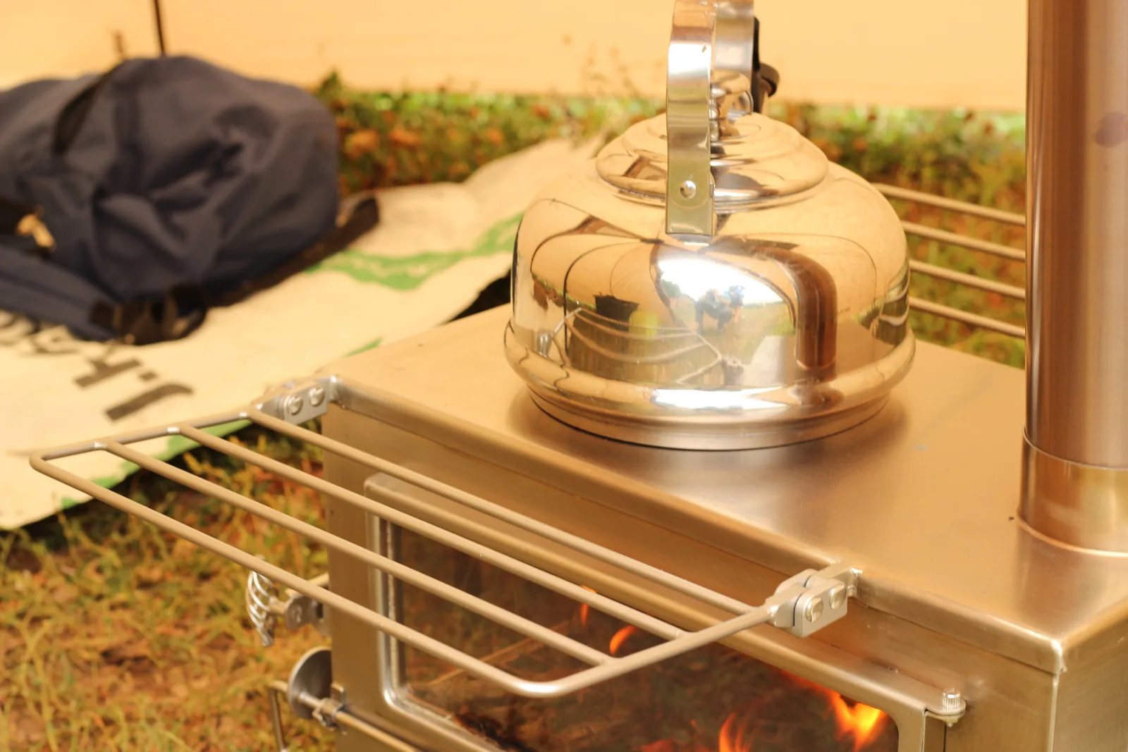 The kettle heating on the stove with the tent wall and a pack visible behind