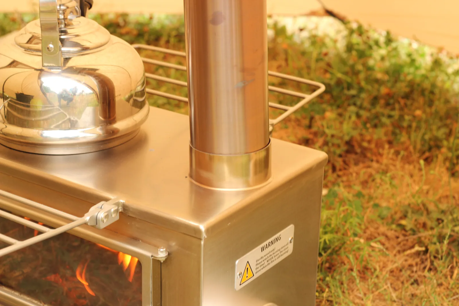 The kettle beside the base of the chimney on the stove top, fire visible through the glass below